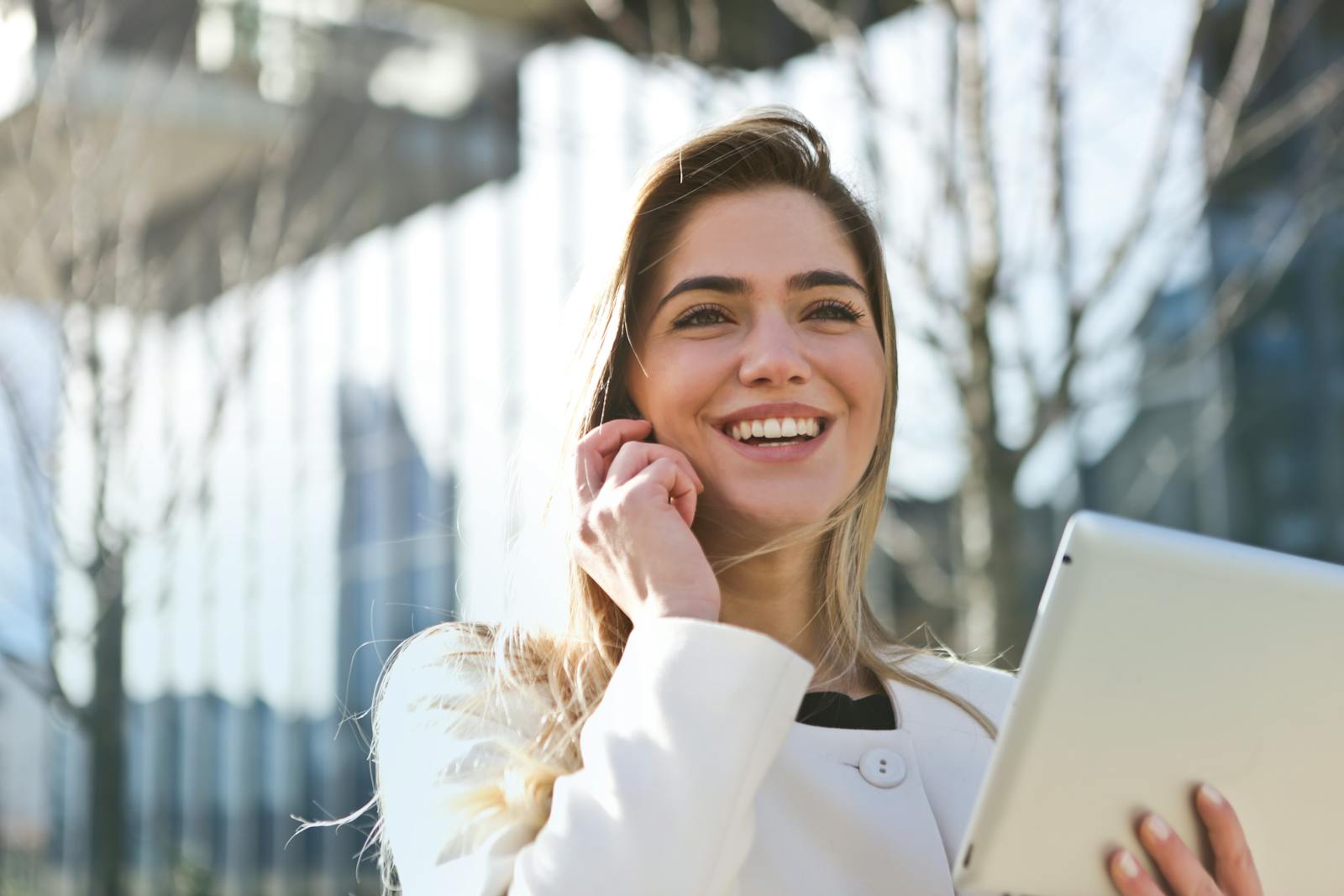 Femme d'affaires confiante utilisant sa tablette et son téléphone, souriant à l'extérieur en plein soleil.